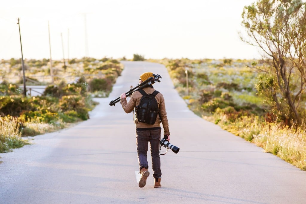 young photographer walking on desert road with tripod on his shoulder picture id696578902 image 